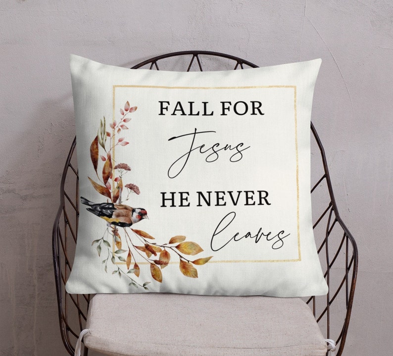 Puede incluir: Una almohada blanca con un marco dorado y un dise&ntilde;o de acuarela de hojas de oto&ntilde;o y un p&aacute;jaro. El texto "Fall for Jesus He Never Leaves" est&aacute; impreso en negro.