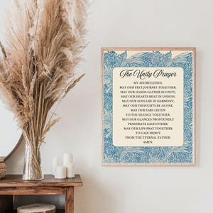 May include: A framed print of "The Unity Prayer" with a blue floral border. The text is in elegant script and block letters on a cream background. The print is displayed on a white wall, next to a vase of dried flowers and candles.