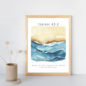 Op de afbeelding: Een ingelijst afdruk met een aquarel van blauwe golven en een beige achtergrond. De afdruk bevat de tekst "ISAIAH 43:2" en het citaat "WHEN YOU PASS THROUGH THE WATERS I WILL BE WITH YOU."