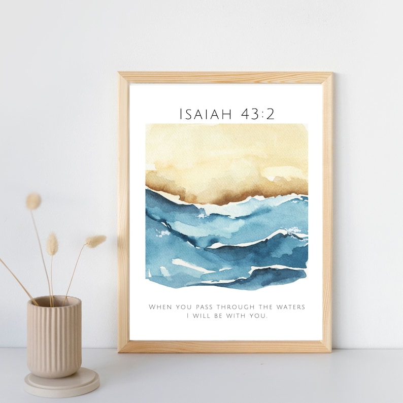 Op de afbeelding: Een ingelijst afdruk met een aquarel van blauwe golven en een beige achtergrond. De afdruk bevat de tekst "ISAIAH 43:2" en het citaat "WHEN YOU PASS THROUGH THE WATERS I WILL BE WITH YOU."