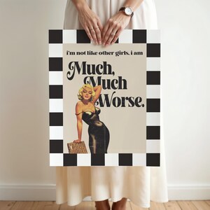 May include: A framed print featuring a vintage-style image of a woman in a black dress, with the text "Much, Much Worse." The frame has a black and white checkered pattern. The woman is blonde and leaning on a basket.