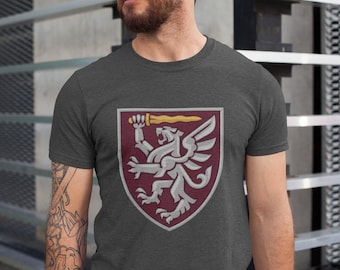 Könnte beinhalten: Ein dunkelgraues T-Shirt mit einem burgunderfarbenen Schild, auf dem ein silberner Greif mit einem goldenen Schwert zu sehen ist.