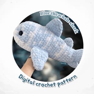 May include: A light blue and white crocheted whale shark plushie. The plushie has a rounded shape with fins and a tail. The text "Blue the whale shark" and "Digital crochet pattern" are displayed in a circular frame.