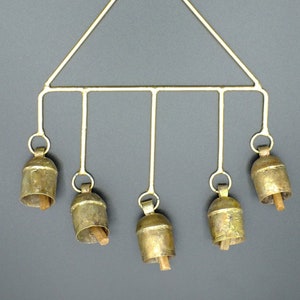 Peut inclure: Un carillon en métal doré avec cinq cloches suspendues à un cadre triangulaire. Les cloches sont en laiton et ont une finition martelée. Le carillon mesure environ 30 cm de haut.