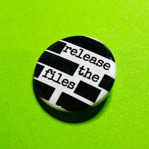 K&ouml;nnte beinhalten: Ein runder Button mit einem schwarz-wei&szlig;en Design und dem Text "release the files" in einer Schreibmaschinenschrift. Der Button hat eine gl&auml;nzende Oberfl&auml;che und befindet sich auf einem leuchtend gr&uuml;nen Hintergrund.