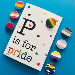 Könnte beinhalten: Eine weiße Karte mit dem Text "P is for pride" in Regenbogenfarben, umgeben von bunten herzförmigen Konfetti und Buttons mit Pride-Flaggen. Die Buttons zeigen verschiedene Pride-Flaggen, darunter Regenbogen-, Transgender- und Bisexuellen-Flaggen.