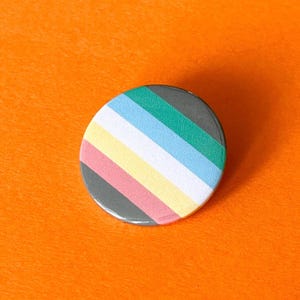 May include: A round button with a striped design in shades of grey, pink, yellow, light blue, and green. The button is on an orange background.