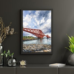 May include: Watercolor painting of a red bridge spanning a body of water under a cloudy sky. The bridge is framed in a black rectangular frame. The foreground shows a rocky shoreline.