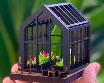 May include: A miniature black wooden greenhouse with a glass roof and sides. The greenhouse is filled with small green plants and pink flowers. There are tiny figures of people inside the greenhouse.