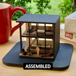 May include: A black and wood model of a modern house with a black base and the word "ASSEMBLED" printed on the base.