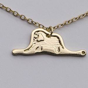 May include: A gold necklace with a pendant shaped like an elephant standing on a thin line. The elephant is detailed with textured lines and a small heart shape on its chest.
