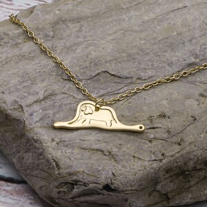 May include: A gold necklace with a pendant shaped like the 'The Giving Tree' illustration. The pendant features a tree with a trunk and branches, and a person sitting on the trunk.