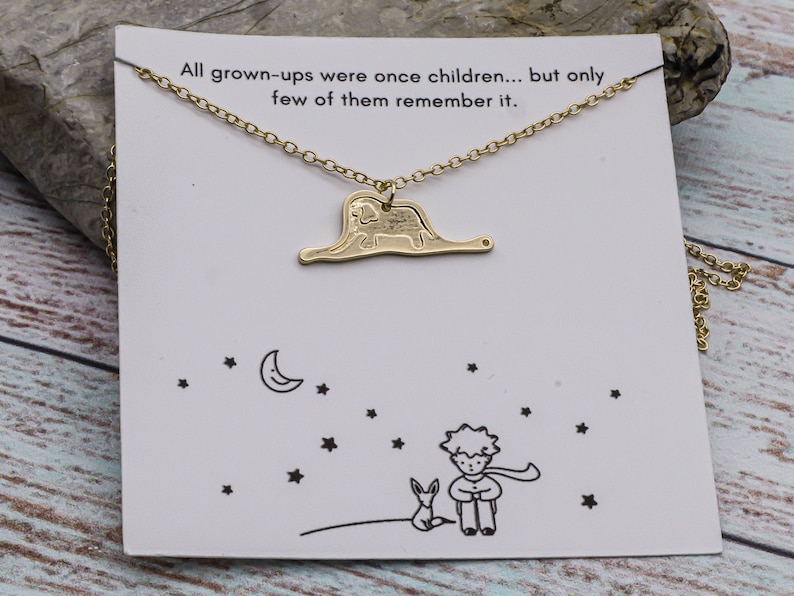 May include: Gold necklace with a charm of a small prince and a fox, and a quote from The Little Prince: "All grown-ups were once children... but only few of them remember it."