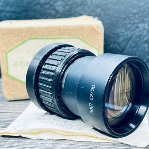 Op de afbeelding: Een zwarte camera lens met een zilveren band en de tekst "16KП-1:2/50".