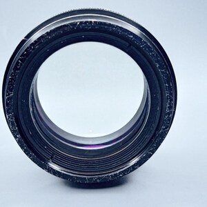 May include: A black camera lens with a silver ring around the edge. The lens has a clear glass front and a series of black rings around the edge.