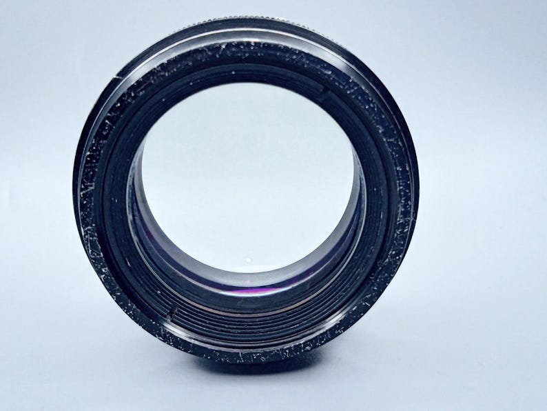 May include: A black camera lens with a silver ring around the edge. The lens has a clear glass front and a series of black rings around the edge.