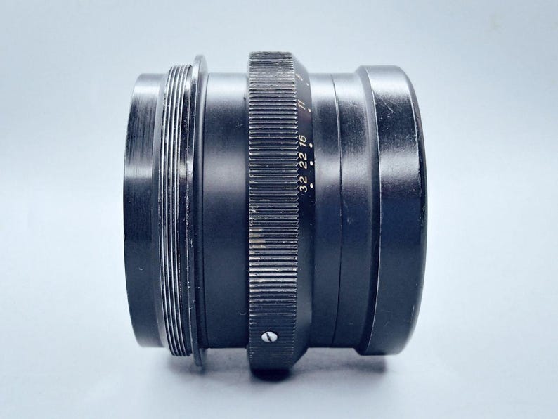 May include: A black camera lens with a silver aperture ring and markings that read "32 22 16".