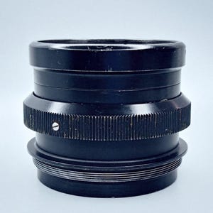 May include: A black camera lens with a ribbed metal ring and a series of concentric rings around the base.