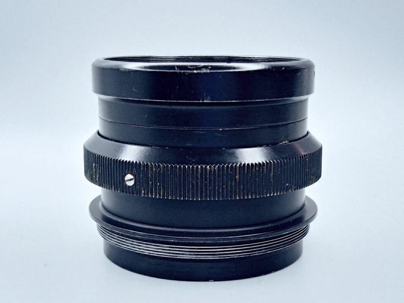 May include: A black camera lens with a ribbed metal ring and a series of concentric rings around the base.