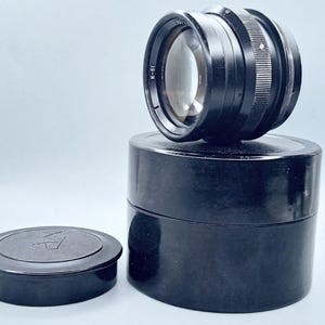 May include: A black camera lens with a black lens cap and a black storage case. The lens has the text "I-51" printed on the side.
