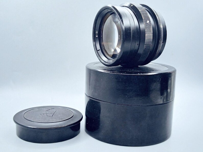 May include: A black camera lens with a black lens cap and a black storage case. The lens has the text "I-51" printed on the side.