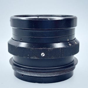 May include: A black camera lens with a series of rings and a screw on the side.