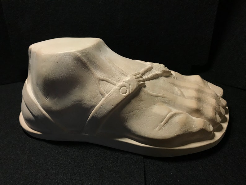 K&ouml;nnte beinhalten: Wei&szlig;e Gips-Skulptur eines Fu&szlig;es, der eine Sandale tr&auml;gt. Die Sandale hat einen Riemen &uuml;ber dem Fu&szlig; mit einer Schnalle.