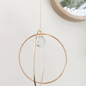 May include: A gold metal sphere mobile with a crystal prism hanging from the center. The mobile is suspended from a gold chain.