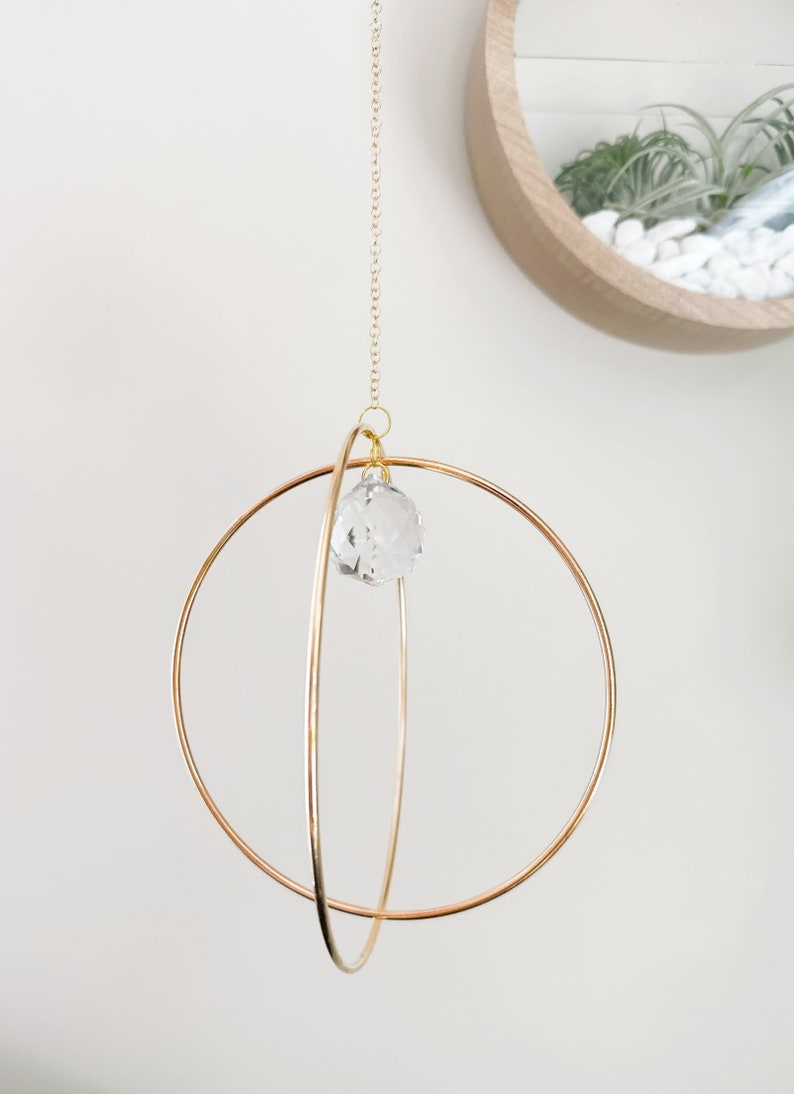 May include: A gold metal sphere mobile with a crystal prism hanging from the center. The mobile is suspended from a gold chain.