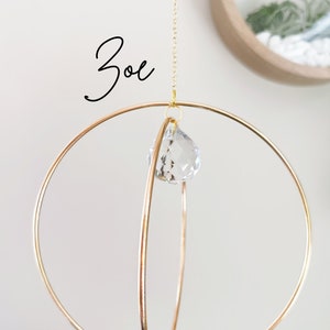May include: A gold metal sphere mobile with a crystal prism hanging from the center. The mobile is suspended from a gold chain.