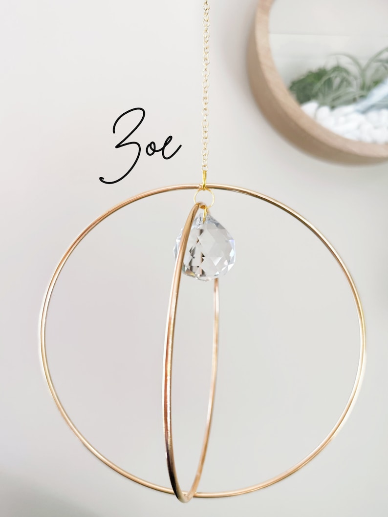 May include: A gold metal sphere mobile with a crystal prism hanging from the center. The mobile is suspended from a gold chain.