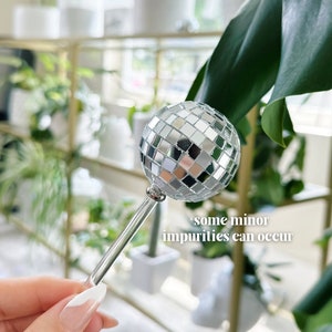 May include: A silver disco ball on a clear glass stick. The disco ball is made up of many small mirrored squares. *some minor impurities can occur*