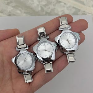May include: Three silver star-shaped wristwatches. Each watch has a silver face with black numerals at the 12, 3, 6, and 9 o'clock positions. The watch bands are silver and have a rectangular clasp.
