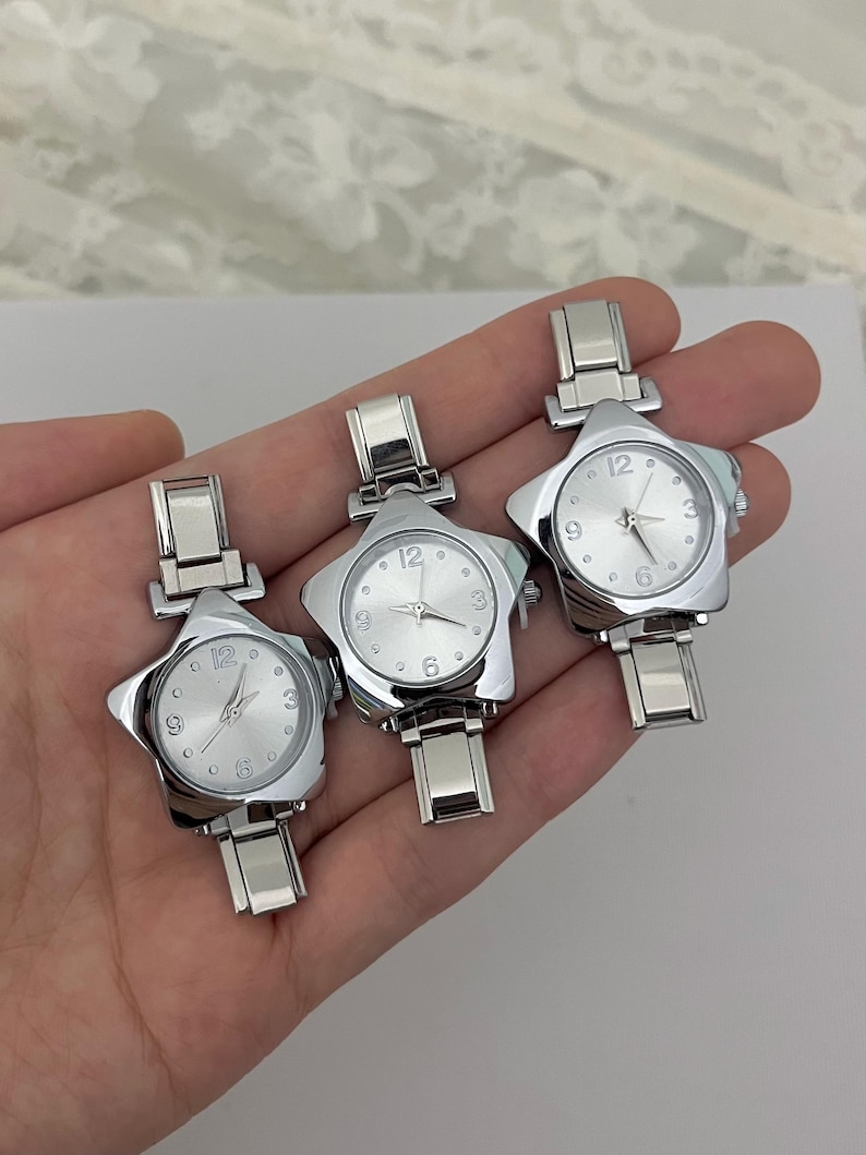 May include: Three silver star-shaped wristwatches. Each watch has a silver face with black numerals at the 12, 3, 6, and 9 o'clock positions. The watch bands are silver and have a rectangular clasp.
