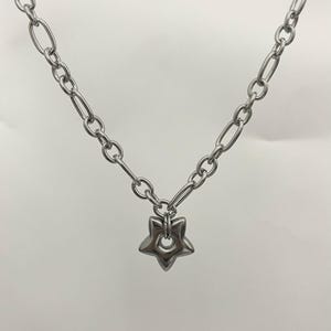 May include: A silver-toned metal chain necklace featuring a series of alternating oval and circular links. A single, polished, five-pointed star-shaped pendant with a circular cutout in the center hangs from the bottom of the chain.