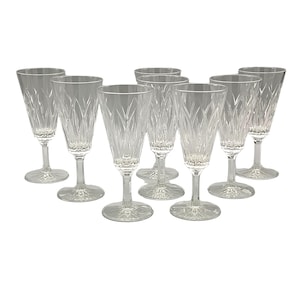 Puede incluir: Un conjunto de nueve copas de champán de cristal transparente. Cada copa presenta una copa alta y delgada con un delicado patrón grabado y un tallo largo. Las copas están dispuestas sobre un fondo blanco.