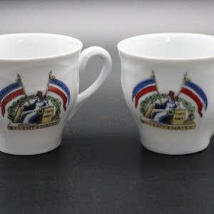Könnte beinhalten: Zwei weiße Keramikbecher mit Henkeln. Jeder Becher hat ein farbenfrohes Emblem mit Flaggen, einer sitzenden Figur und dem Text "Bicentenaire Paris 1789-1989". Die Becher haben ein klassisches Design.