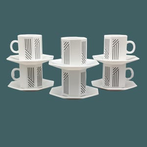 Peut inclure: Ensemble de six tasses à café et soucoupes en céramique blanche avec un motif géométrique noir. Les tasses et les soucoupes sont empilées par paires.