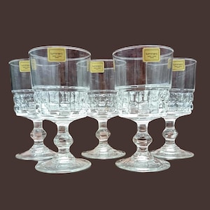 Peut inclure: Six verres Luminarc transparents avec une partie inférieure texturée et à motifs et une partie supérieure lisse. Chaque verre a un pied et une base ronde. L'étiquette Luminarc est visible sur chaque verre. Les verres sont disposés en demi-cercle.