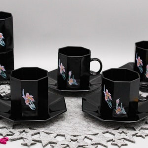 Peut inclure: Ensemble de six tasses à thé et soucoupes noires avec des motifs floraux. Les tasses et les soucoupes ont une forme géométrique et sont décorées de fleurs roses et blanches.