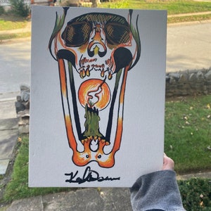 May include: A hand-painted canvas featuring a skull with a candle inside its mouth. The skull is orange and yellow, and the candle is green. The canvas is signed "Kali Dawn".