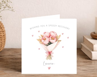 May include: A white greeting card featuring a watercolor illustration of a pink peony bouquet wrapped in paper with a pink ribbon. The text reads WISHING YOU A SPEEDY RECOVERY and the name Lauren in black script, surrounded by small pink hearts.