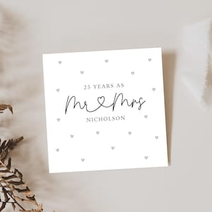Op de afbeelding: Een witte kaart met zwarte tekst die "25 Years as Mr & Mrs Nicholson" luidt, met een klein hartje tussen de woorden "Mr" en "Mrs". De kaart is versierd met kleine grijze hartjes.