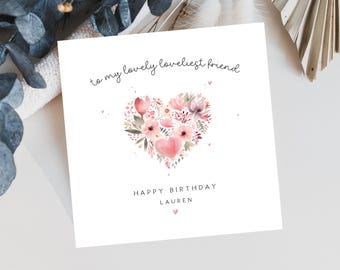 May include: A white greeting card with a watercolor heart-shaped floral design. The heart is filled with pink, red, and purple flowers and green leaves. The card reads "to my lovely loveliest friend" and "Happy Birthday Lauren".
