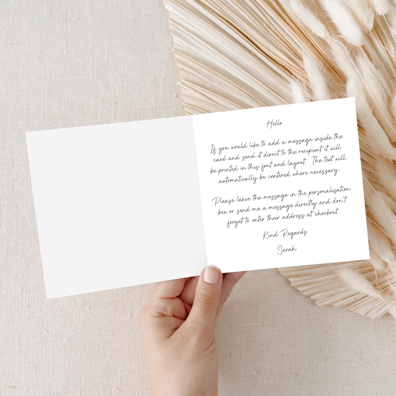 Puede incluir: Una tarjeta de felicitaci&oacute;n blanca abierta, con texto manuscrito en tinta negra. El texto proporciona instrucciones para agregar un mensaje y enviarlo directamente al destinatario. La tarjeta est&aacute; sostenida por una mano, sobre un fondo neutro.