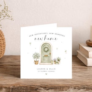 Op de afbeelding: Een vierkante wenskaart met een aquarelillustratie van een boogvormige saliegroene deur met een krans, potplanten en de tekst "NEW ADVENTURES, NEW MEMORIES new home" erboven, en "LAUREN & OLLIE 35 FAIRWAY AVENUE" onder de deur.