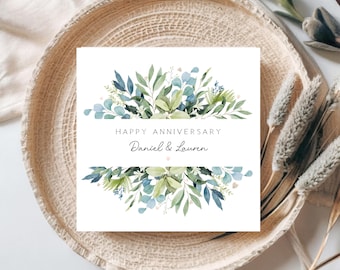 May include: A white card with a watercolor illustration of green and blue leaves. The text "Happy Anniversary Daniel & Lauren" is printed on the card.