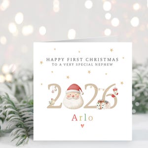 Op de afbeelding: Een vierkante wenskaart met de tekst Happy First Christmas To A Very Special Nephew boven het jaartal 2026. Het cijfer nul is vervangen door een kerstmangezicht met een rode muts. De naam Arlo staat eronder met een klein rood hartje.