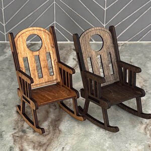 Peut inclure: Deux petites chaises &agrave; bascule en bois. L'une est brun clair, l'autre est brun fonc&eacute;. Les deux ont un design de chaise &agrave; bascule classique avec un dossier &agrave; lattes et des accoudoirs. Les chaises sont en bois et sont probablement des objets d&eacute;coratifs.