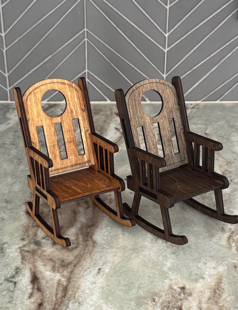 Peut inclure: Deux petites chaises &agrave; bascule en bois. L'une est brun clair, l'autre est brun fonc&eacute;. Les deux ont un design de chaise &agrave; bascule classique avec un dossier &agrave; lattes et des accoudoirs. Les chaises sont en bois et sont probablement des objets d&eacute;coratifs.